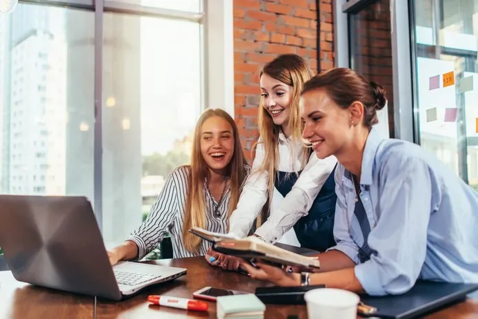 Three women collaborating around a laptop in a bright office