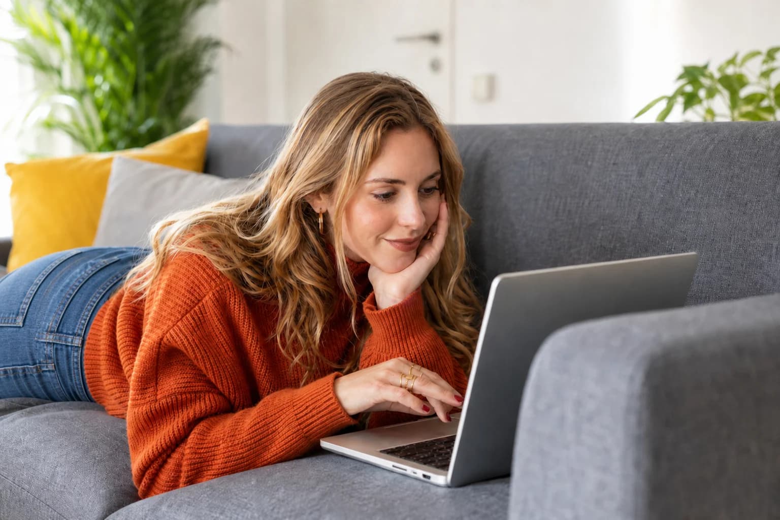 Woman in an orange sweater working on a laptop on the couch